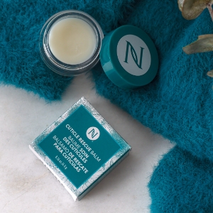 Images of Cuticle Rescue Balm, both an open jar and the box, atop a blue towel.